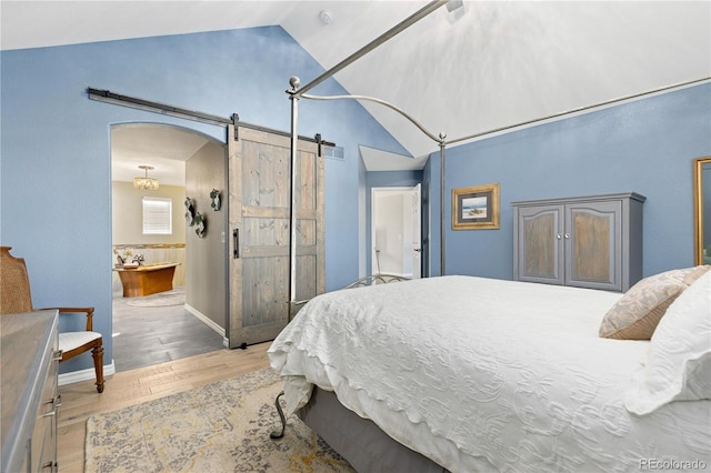 bedroom featuring high vaulted ceiling, light hardwood / wood-style floors, a barn door, and ensuite bathroom