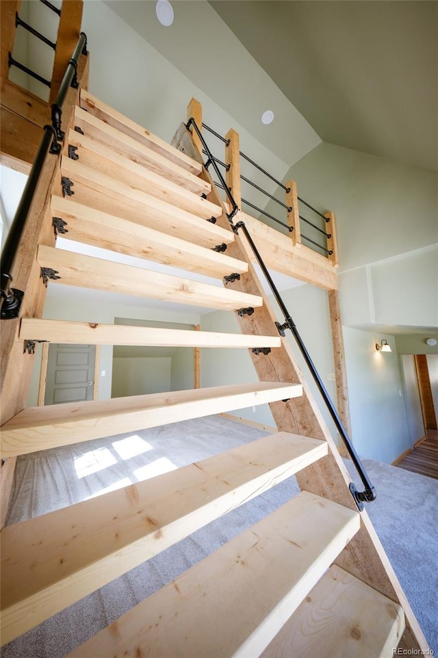 stairway with carpet flooring and high vaulted ceiling