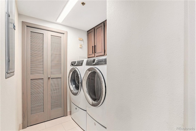 clothes washing area featuring light tile patterned floors, washer and dryer, and cabinets