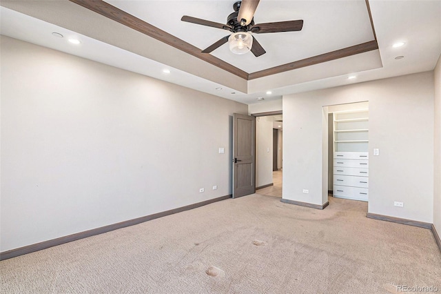 unfurnished bedroom with a spacious closet, light carpet, a closet, ceiling fan, and a tray ceiling