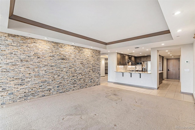 unfurnished living room with light tile patterned floors, crown molding, a tray ceiling, and sink