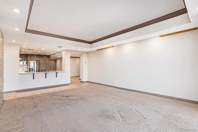 unfurnished living room with a tray ceiling, sink, light tile patterned floors, and crown molding