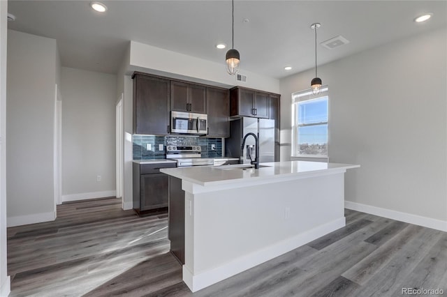 kitchen featuring hardwood / wood-style flooring, stainless steel appliances, decorative light fixtures, a kitchen island with sink, and sink