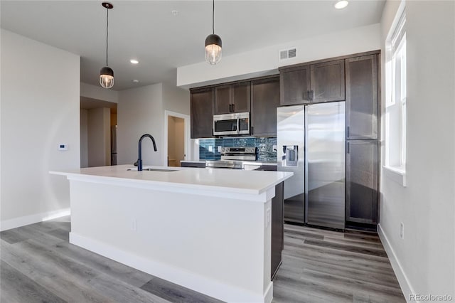 kitchen featuring an island with sink, stainless steel appliances, hanging light fixtures, and sink