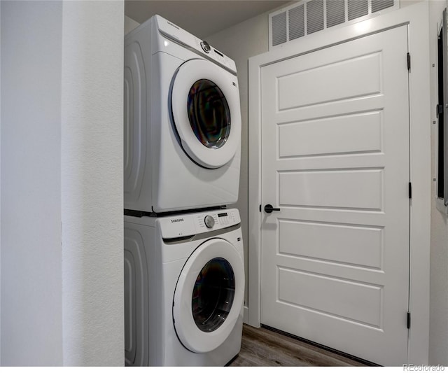 laundry room featuring stacked washer and dryer and dark hardwood / wood-style flooring