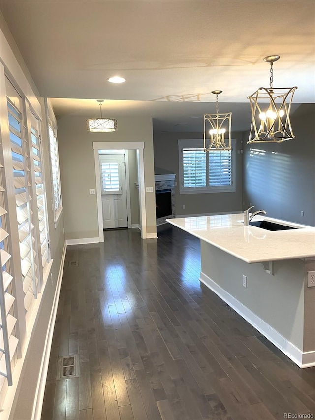 kitchen featuring sink, a center island with sink, a notable chandelier, dark hardwood / wood-style floors, and hanging light fixtures