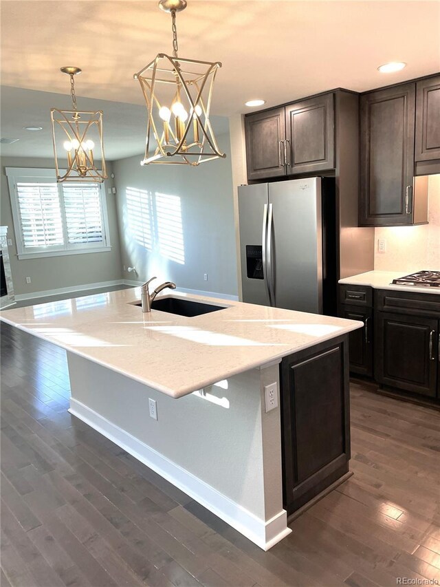 kitchen with appliances with stainless steel finishes, dark brown cabinetry, light stone counters, and sink