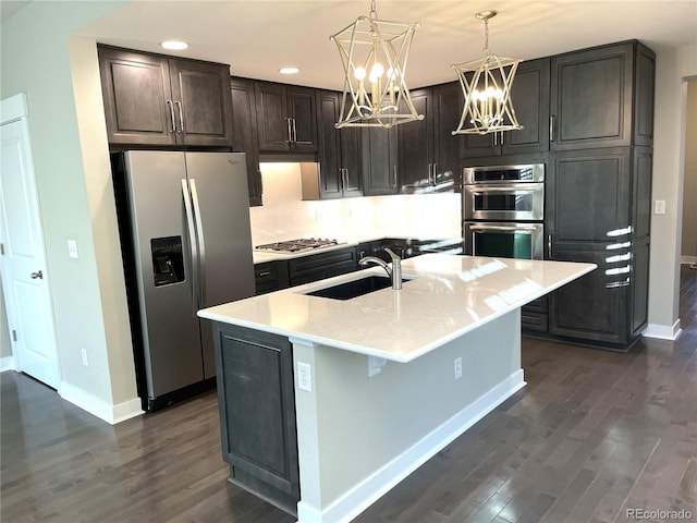 kitchen with stainless steel appliances, sink, a center island with sink, an inviting chandelier, and dark hardwood / wood-style floors