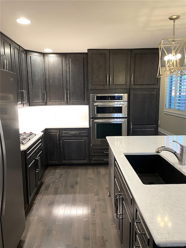 kitchen featuring pendant lighting, dark wood-type flooring, sink, light stone counters, and stainless steel appliances