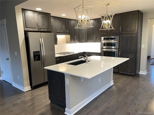 kitchen with sink, stainless steel appliances, an inviting chandelier, dark hardwood / wood-style flooring, and an island with sink