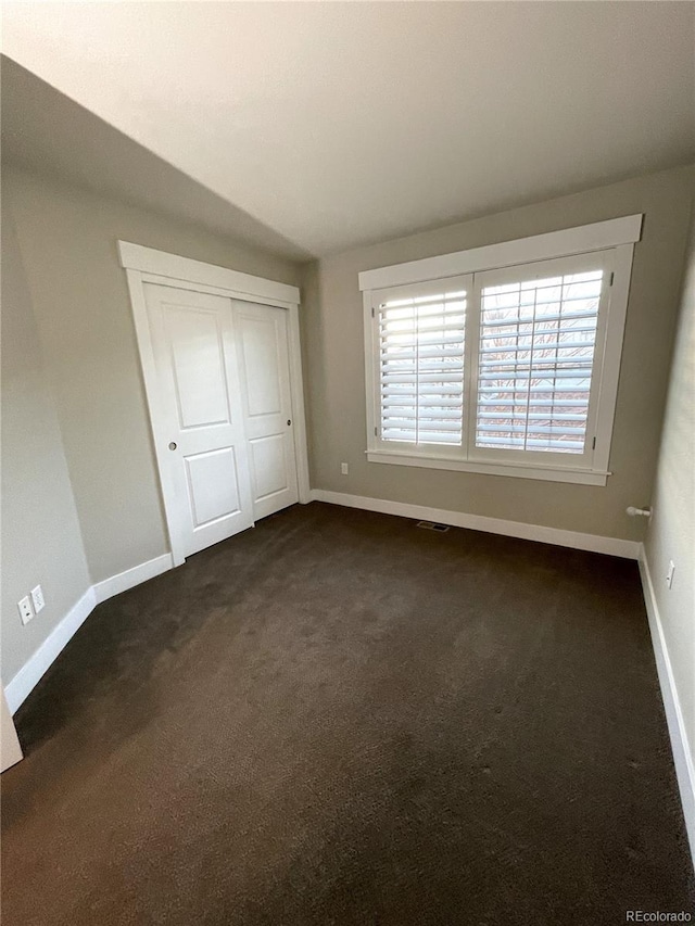 unfurnished bedroom with a closet and dark colored carpet