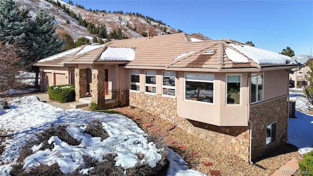 view of front of property featuring a tile roof, stucco siding, a garage, stone siding, and a mountain view