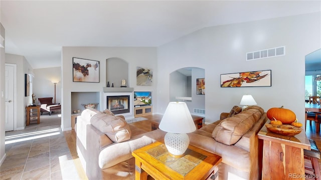 living room with a glass covered fireplace, arched walkways, visible vents, and high vaulted ceiling