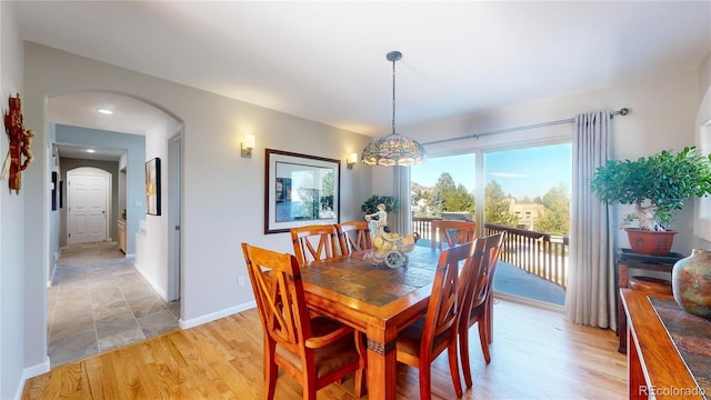 dining area with light wood-style floors, arched walkways, and baseboards