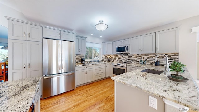 kitchen with light stone countertops, decorative backsplash, appliances with stainless steel finishes, a peninsula, and a sink