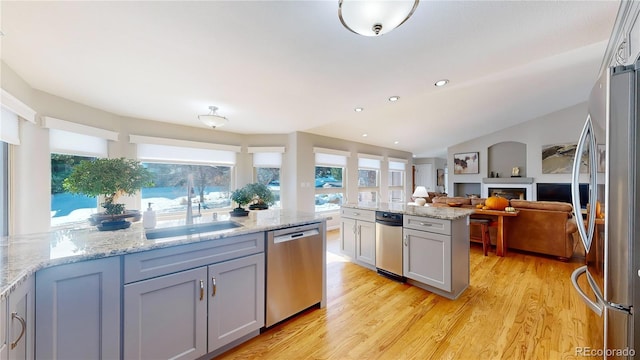 kitchen with light wood finished floors, a fireplace, appliances with stainless steel finishes, and a sink