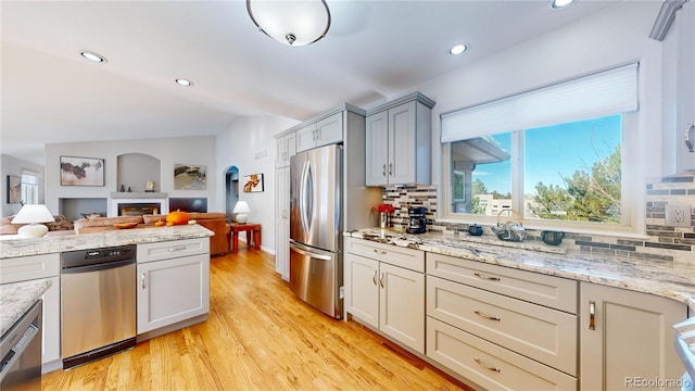 kitchen with tasteful backsplash, open floor plan, arched walkways, light wood-style floors, and appliances with stainless steel finishes