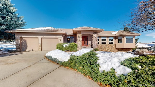 prairie-style home with stone siding, stucco siding, driveway, and a garage