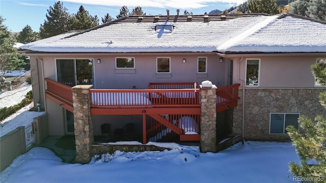 snow covered rear of property featuring stairway, stone siding, and a wooden deck