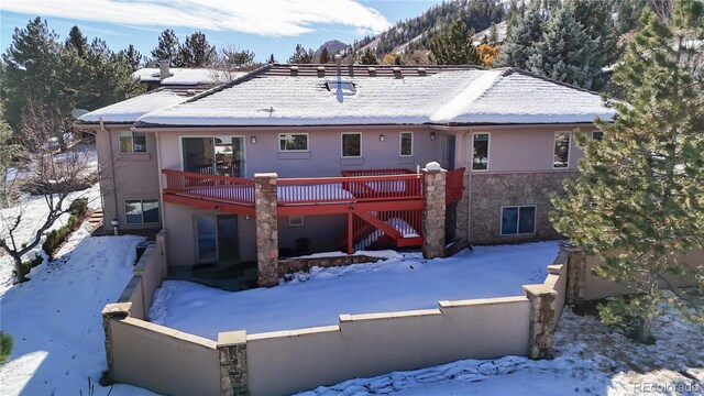 snow covered rear of property featuring a deck, stairway, and a fenced front yard