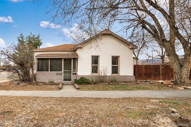 bungalow-style home featuring a sunroom, stucco siding, and fence