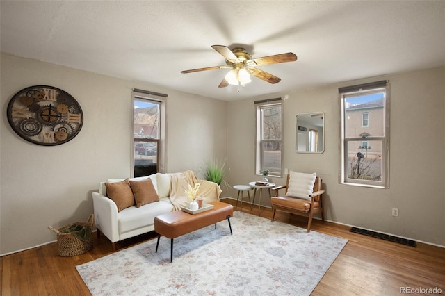 living room with visible vents, wood finished floors, and ceiling fan