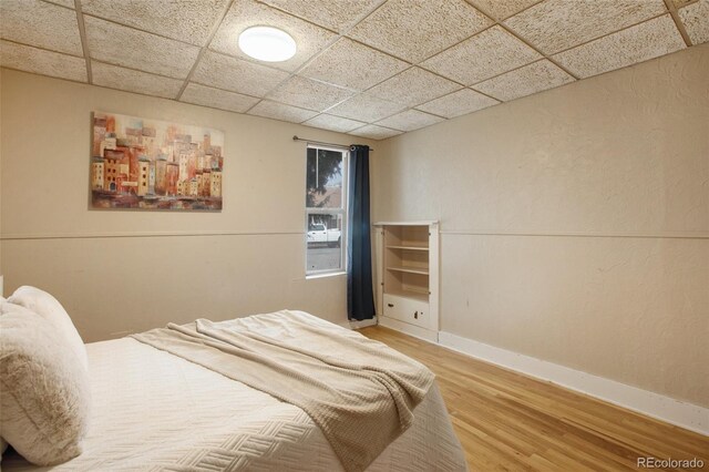 bedroom featuring baseboards, a paneled ceiling, and light wood-type flooring