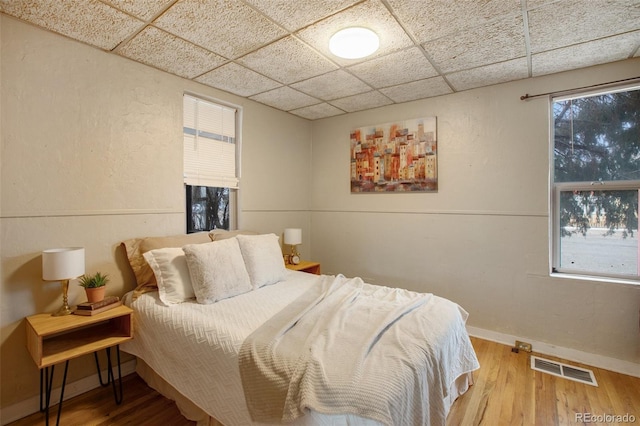 bedroom with baseboards, visible vents, a paneled ceiling, and wood finished floors