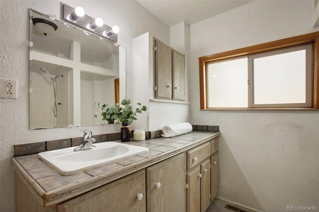full bathroom with a textured wall, a shower, and vanity