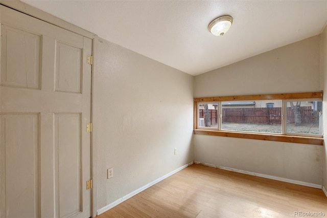 unfurnished room featuring baseboards, lofted ceiling, and light wood-style floors
