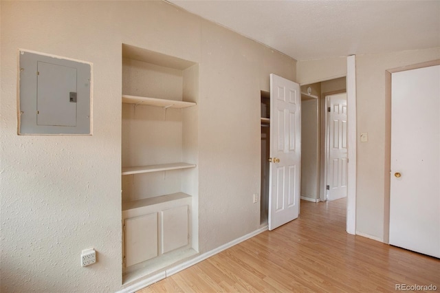 unfurnished bedroom featuring electric panel, baseboards, a closet, and wood finished floors