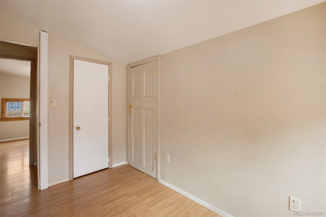 unfurnished bedroom with baseboards, lofted ceiling, and light wood-style flooring