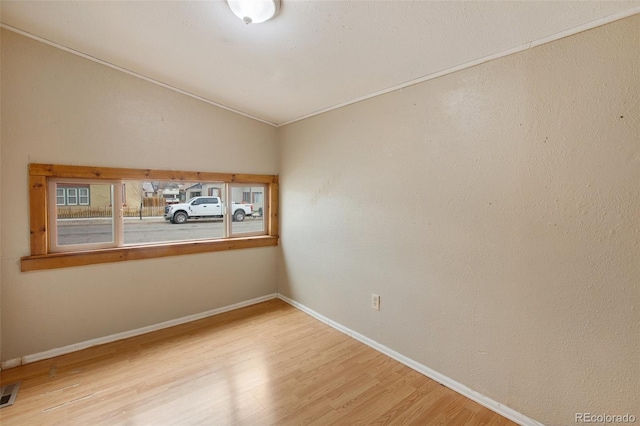 spare room with wood finished floors, baseboards, vaulted ceiling, and visible vents