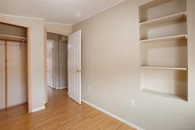 unfurnished bedroom featuring baseboards, ornamental molding, wood finished floors, and a closet