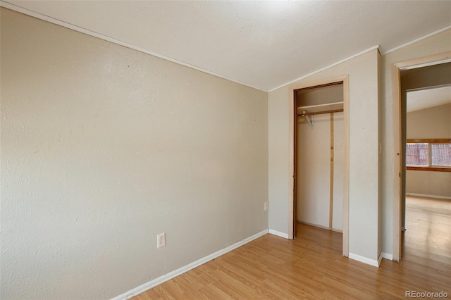 unfurnished bedroom featuring baseboards, lofted ceiling, crown molding, and light wood finished floors