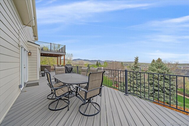wooden deck with a mountain view, outdoor dining area, and a grill