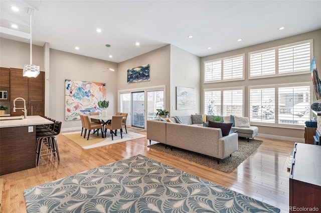 living room with a high ceiling, sink, and light hardwood / wood-style flooring