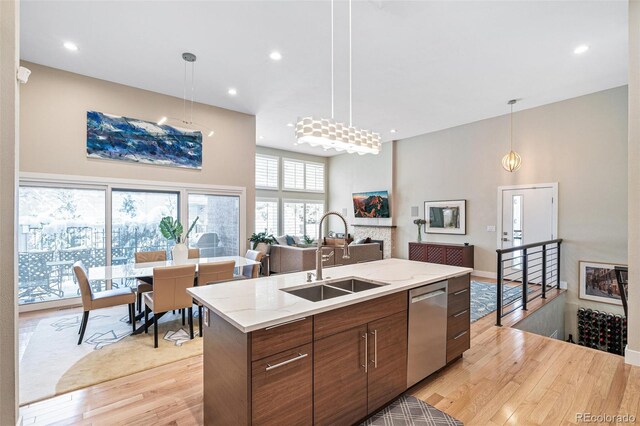 kitchen featuring pendant lighting, dishwasher, sink, light wood-type flooring, and a center island with sink