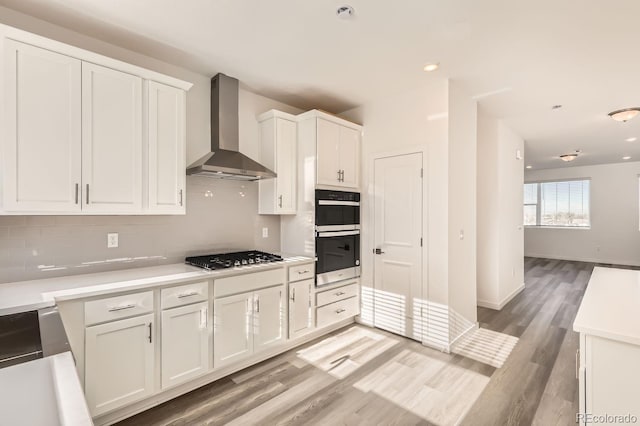 kitchen featuring white cabinetry, stainless steel gas cooktop, wall chimney exhaust hood, light wood-type flooring, and tasteful backsplash