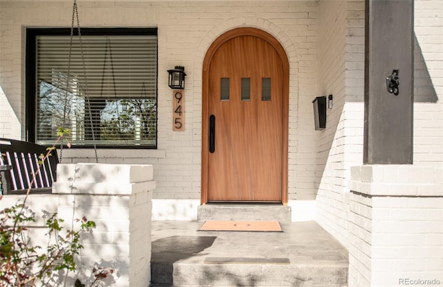 doorway to property with a porch and brick siding