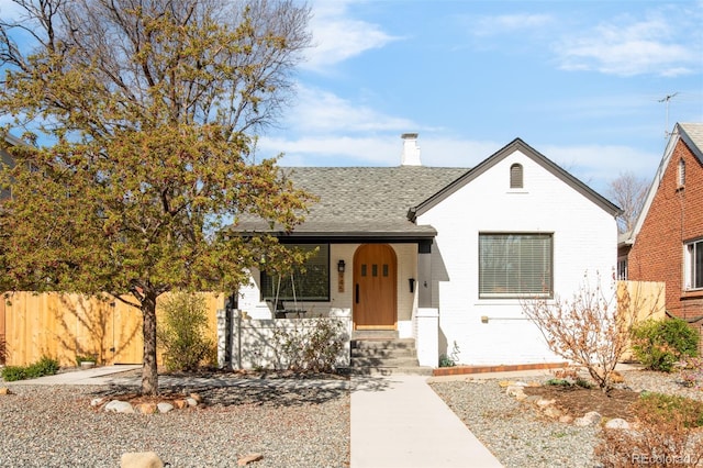 bungalow-style home featuring a chimney, brick siding, fence, a shingled roof, and a porch