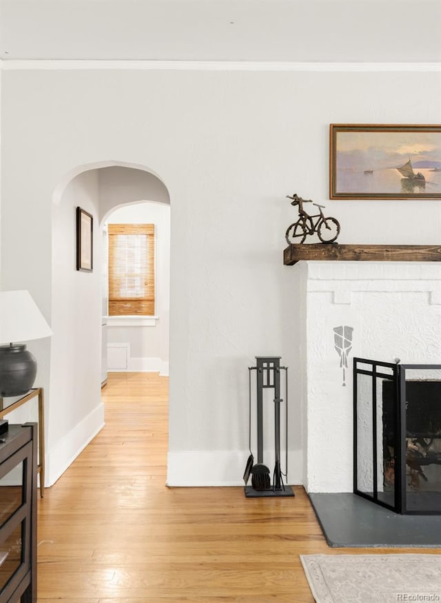 hall featuring ornamental molding, light wood-style flooring, arched walkways, and baseboards
