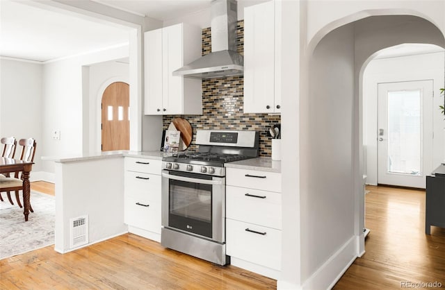 kitchen with stainless steel gas range oven, light wood-style flooring, visible vents, and wall chimney exhaust hood