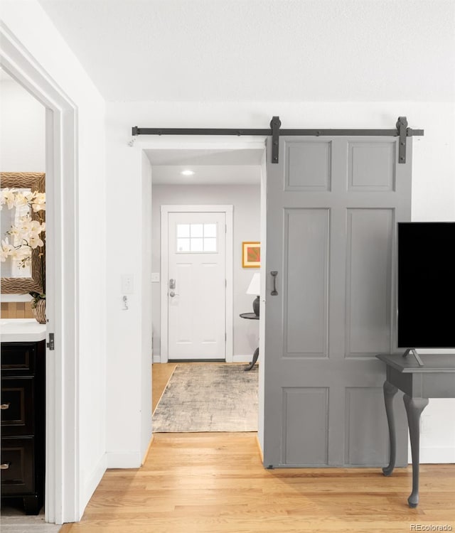 foyer entrance with light wood finished floors, a barn door, and baseboards
