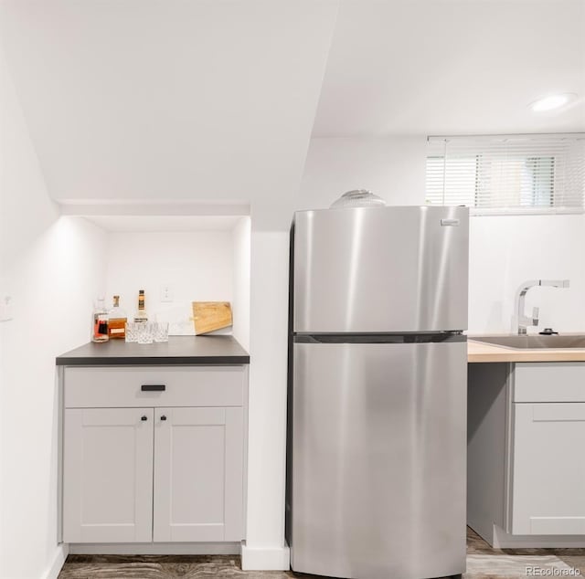 kitchen with a sink, wood finished floors, freestanding refrigerator, white cabinets, and dark countertops