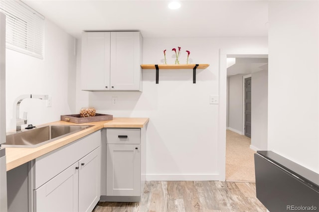 kitchen with white cabinets, light wood-type flooring, baseboards, and a sink