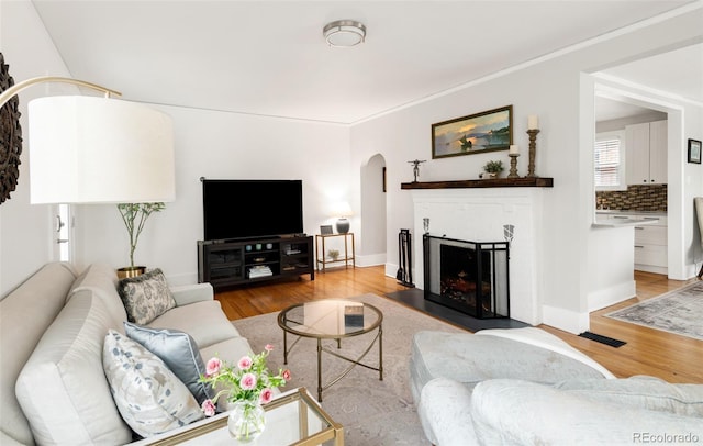 living room featuring a fireplace, light wood-style flooring, arched walkways, and visible vents