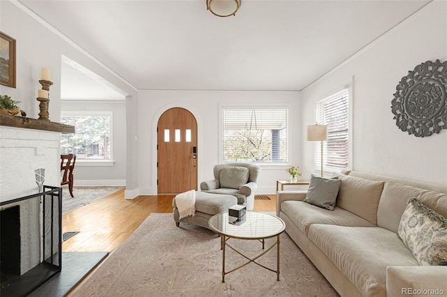 living area with wood finished floors, a fireplace, crown molding, baseboards, and arched walkways