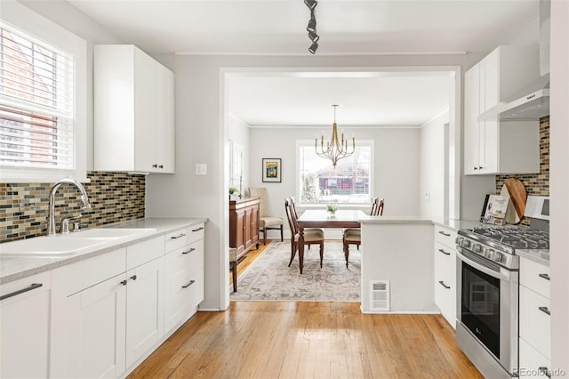 kitchen with stainless steel gas range, a sink, wall chimney exhaust hood, white cabinetry, and visible vents