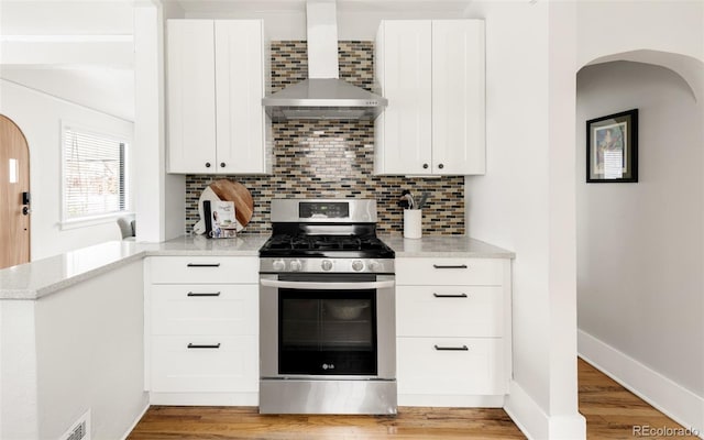 kitchen featuring arched walkways, stainless steel gas range oven, backsplash, and wall chimney exhaust hood